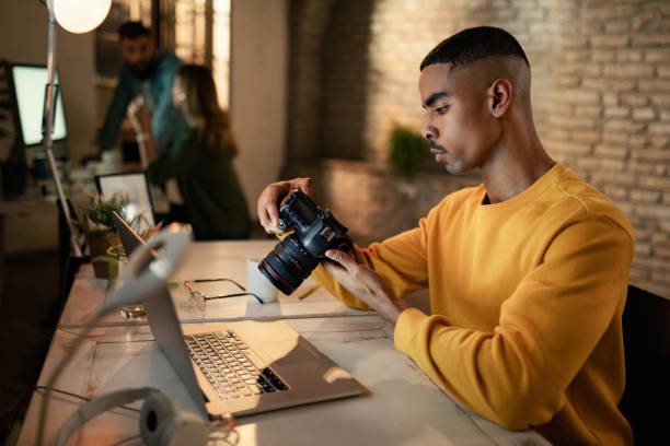 afroamerikanischer fotograf, der bilder vor der kamera betrachtet, während er spät in einem studio arbeitet. - digitalkamera stock-fotos und bilder