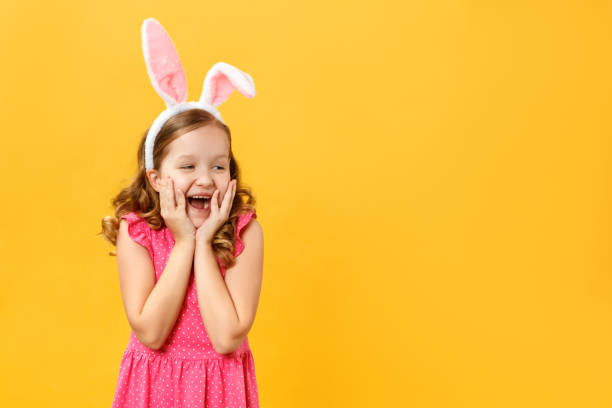 funny little girl in easter bunny ears on a yellow background. the child opened his mouth in surprise and looks at the empty space - surprise child little girls shock imagens e fotografias de stock