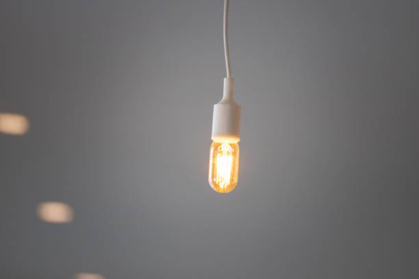 istock white wire and hanging vintage light bulb on grey ceiling background. 1199034336