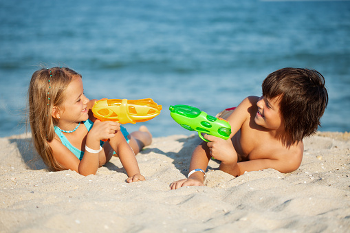 Kids having fun with water pistols on the beach - playing in the sand