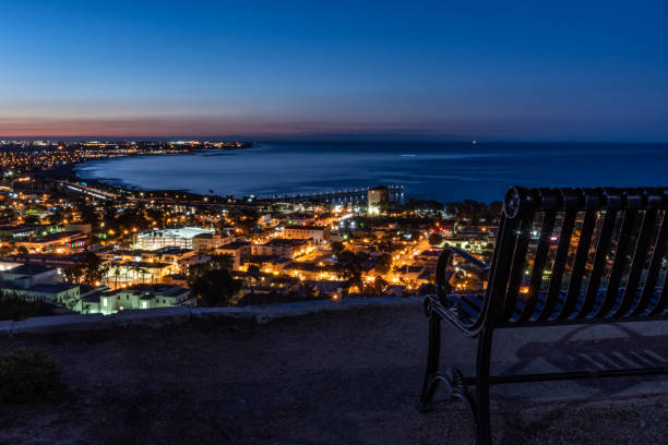Lights of coastal city of Ventura viewed over the park bench at viewpoint as dawn begins to break in the sky.