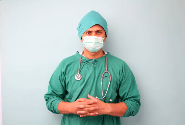mężczyzna chirurg azji, chirurg pokazano stetoskop sobie maskę chirurga, na niebieskim tle w studio. - surgeon isolated paramedic operating room zdjęcia i obrazy z banku zdjęć