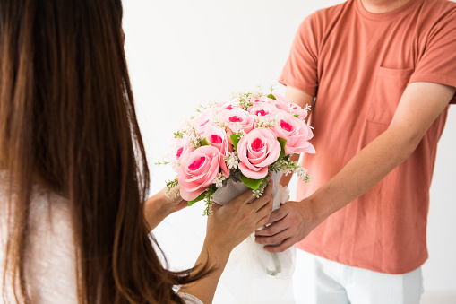 Closeup boyfriend hands giving rose flower bouquet to his girlfriend over white background and copy space for text. Happy couple celebrate 2020 Valentine day.