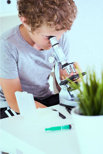 istock Cute elementary schoolboy looking into microscope at his desk in the laboratory. Young scientist making experiments in laboratory. 1199042180