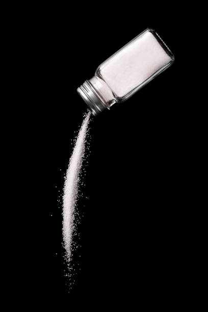 salt is poured from a salt shaker on a black background. - saleiro de mesa imagens e fotografias de stock