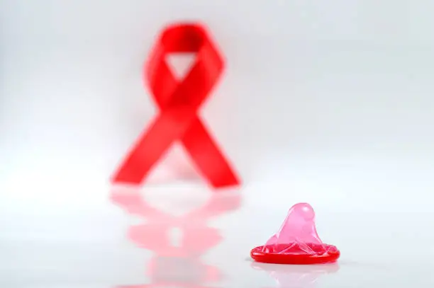 Photo of Aids ribbon and condom on white background.