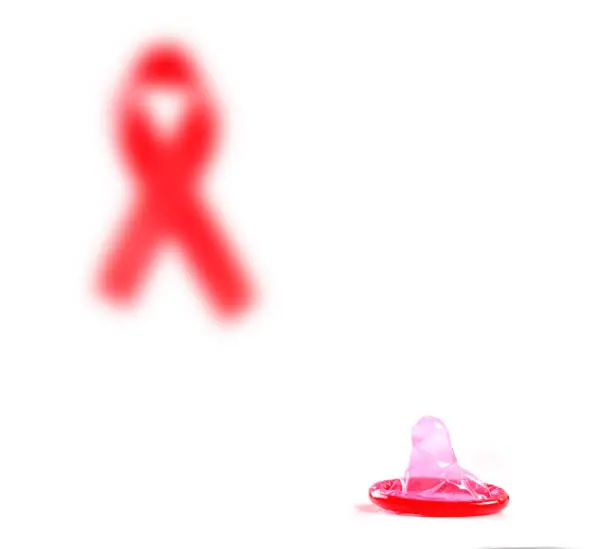 Photo of Aids ribbon and condom on white background.