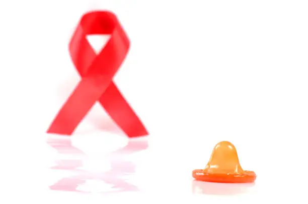 Photo of Aids ribbon and condom on white background.