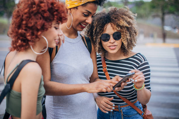 istock Three young women using phone outdoors 1199053182