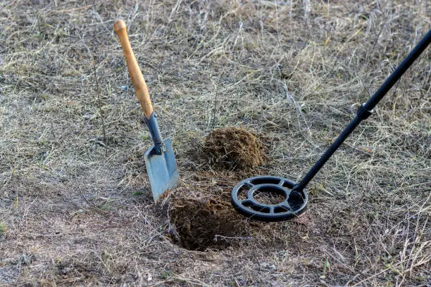 metal detector, mine detector with a shovel near a dug hole in the ground