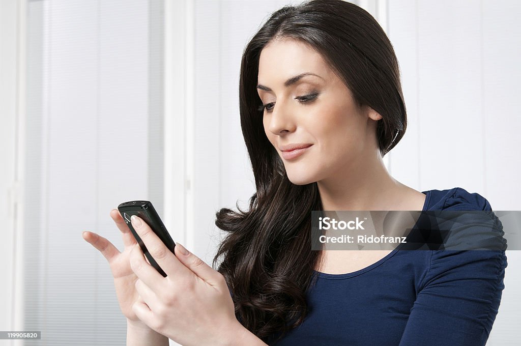 Woman smiling while using smartphone Young beautiful brunette lady touching and browsing her smart phone at home. 20-29 Years Stock Photo