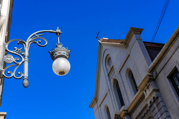 Wrought iron street light with a church at background. Photo taken on a sunny day against deep blue sky. Predominant colors are blue and gray. High resolution outdoors digital capture taken with SONY A7rII and Zeiss Batis 40mm F2.0 CF