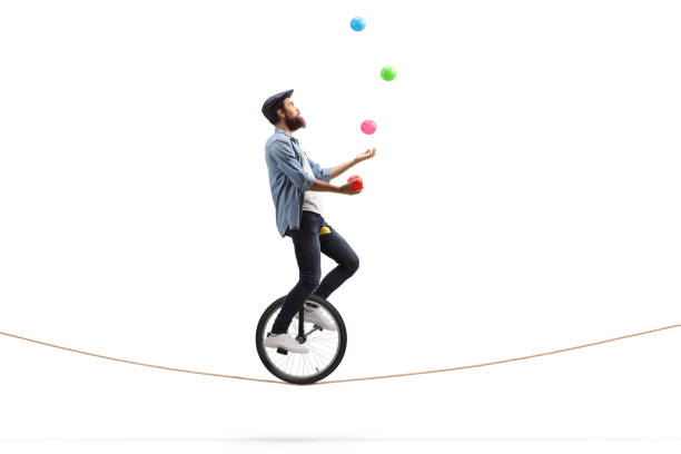 Bearded male hipster juggler with balls riding a unicycle on a rope Full length profile shot of a bearded male hipster juggler with balls riding a unicycle on a rope isolated on white background circus photos stock pictures, royalty-free photos & images