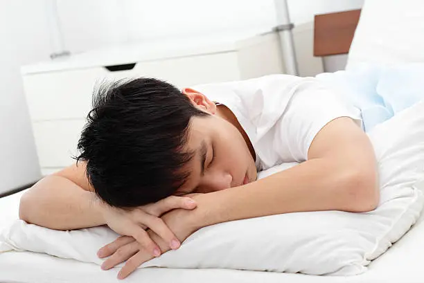A young Asian man sleeping on a bed