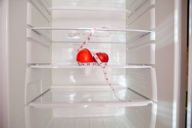 istock Empty refrigerator with a persimmon and green apple and tape measuring on the shelf, diet concept, blurred background 1199068360