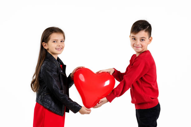 Happy little couple girl and boy holding red heart balloon together isolated on white background. children look at the camera. St. Valentine's Day