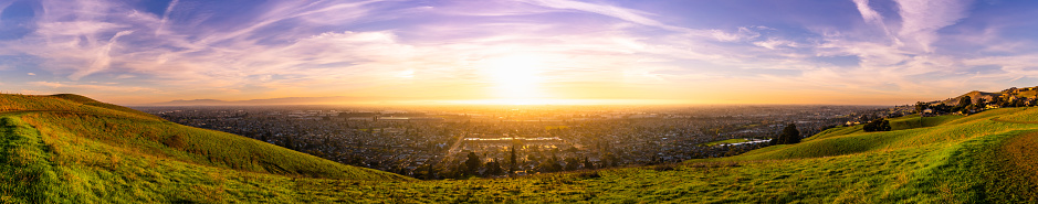 Expansive sunset panorama comprising the cities of east San Francisco bay, Fremont, Hayward and Union City; green hills visible in the foreground; San Francisco Bay Area, California