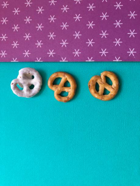 Two pretzels on and one white chocolate covered pretzel on green and purple patterned background