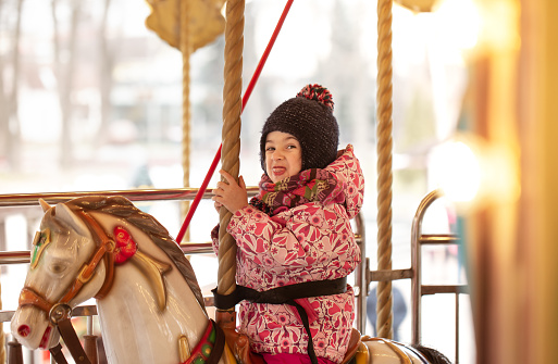 A little girl rides on a carousel, winter holidays.