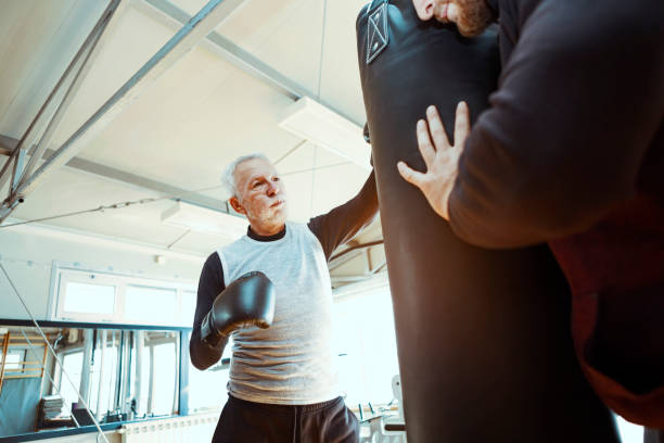 Senior man in gym boxing with trainer Senior in gym boxing old man boxing stock pictures, royalty-free photos & images