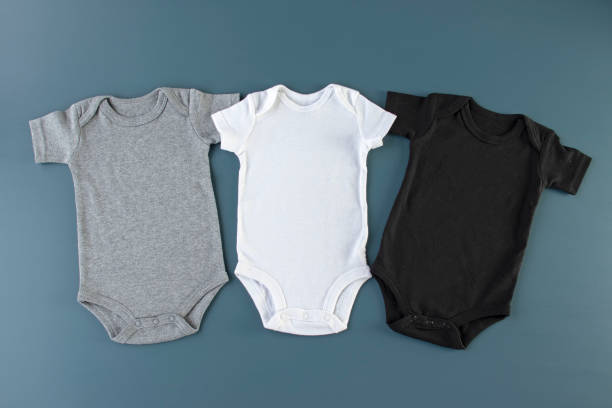 istock Three baby bodysuits on a blue background mockup - 3 baby grows flat lay (white, grey & black) 1199085377