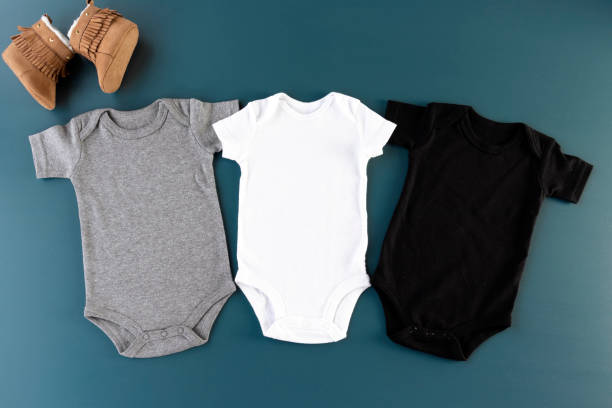 istock Three baby bodysuits on a blue background with shoes mockup - 3 baby grows flat lay (white, grey & black) 1199086606