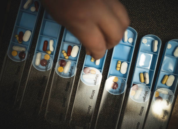 senior man is putting pills and capsules in a 7-day pill organizer - vitamin pill capsule equipment data imagens e fotografias de stock