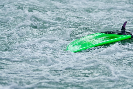 A flipped neon green sufboard on foamy white waters