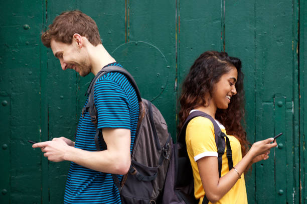 istock male and female students looking at mobile phone while standing back to back 1199097298