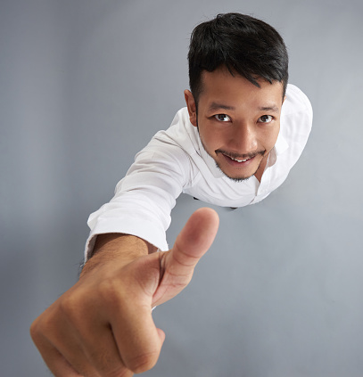 Young asian man show thumb up above top view on gray studio background