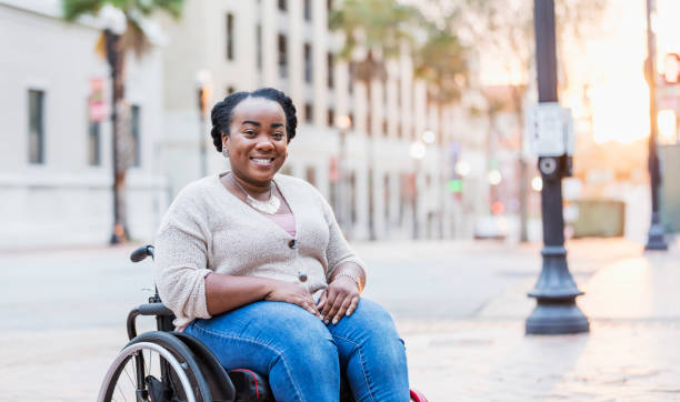 African-American woman with spina bifida A mid adult African-American woman in her 30s in a wheelchair outdoors, in the city, smiling at the camera. She has spina bifida. wheelchair stock pictures, royalty-free photos & images