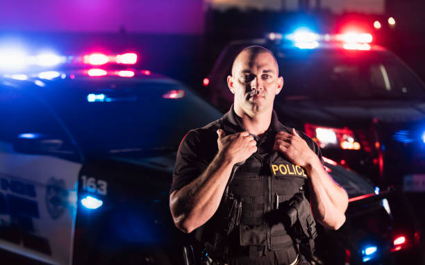 policeman wearing bulletproof vest, by patrol car - policia imagens e fotografias de stock