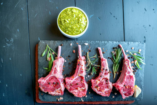 istock Raw Lamb Chops Prepared on a Dark Slate Cutting Board with a Ramekin or Pesto on the side with Rosemary and other herbs 1199113865