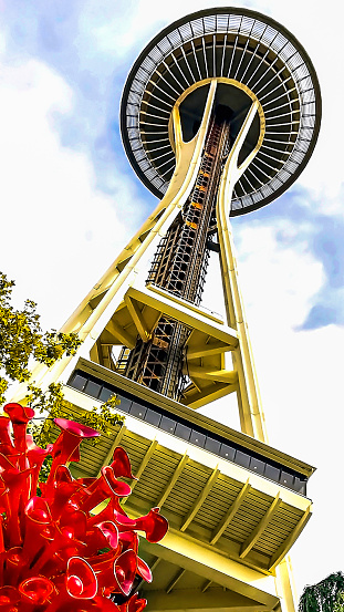 A mesmerizing portrait of the infamous Space Needle in Seattle - towering above the Seattle Proper and Lower Queen Anne neighborhoods - amidst a vibrant red Chihuly original glass sculpture.