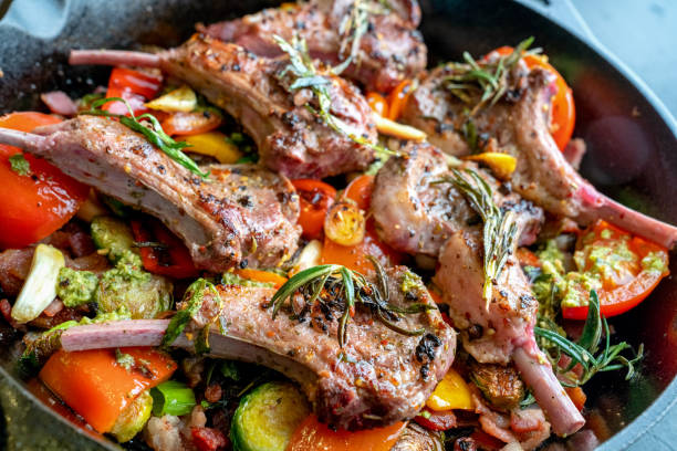 skillet de hierro fundido relleno de chuletas de cordero gourmet y un medley vegetal de coles de bruselas, pimiento, ajo, tomate de puerro, ajo y pesto - rack of lamb chop cutlet rosemary fotografías e imágenes de stock