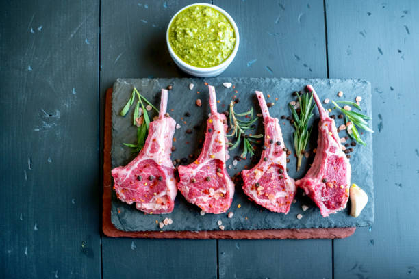 istock Raw Lamb Chops Prepared on a Dark Slate Cutting Board with a Ramekin or Pesto on the side with Rosemary and other herbs 1199115825