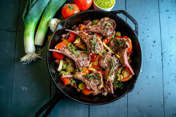 skillet de hierro fundido relleno de chuletas de cordero gourmet y un medley vegetal de coles de bruselas, pimiento, ajo, tomate de puerro, ajo y pesto - dieta paleolítica fotografías e imágenes de stock