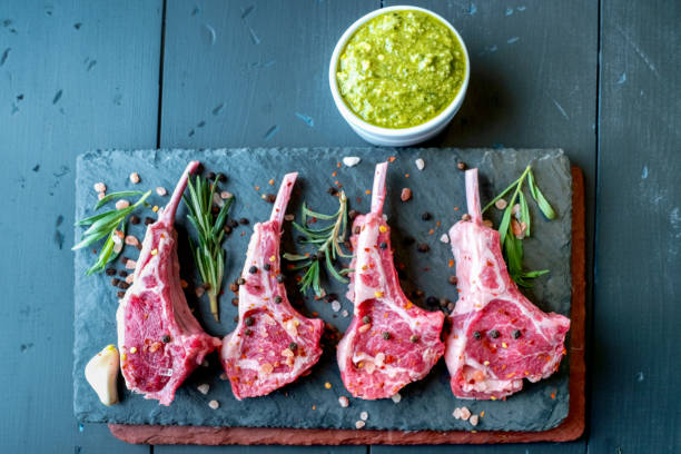 istock Raw Lamb Chops Prepared on a Dark Slate Cutting Board with a Ramekin or Pesto on the side with Rosemary and other herbs 1199118006