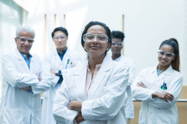 Multi-Ethnic Team of Scientists Portrait stock photo A multi-ethnic group of medical scientists stop and pause for a team portrait before continuing their work. They are each smiling while wearing lab coats and protective eye wear for safety. oncology photos stock pictures, royalty-free photos & images
