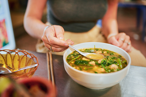 Cropped shot of a woman eating a bowl of prawn noodle soup in a Vietnamese restaurant