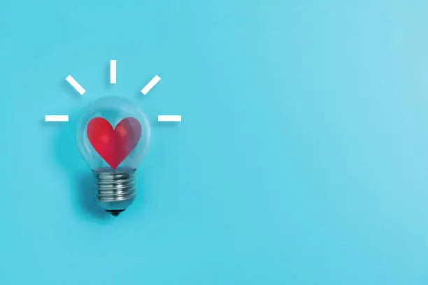 Photo of Red heart in light bulb on blue background with copy space.