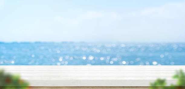 table en bois de planche blanche vide avec le ciel bleu flou et le fond de bokeh de mer avec le premier plan vert de feuille, modèle de maquette pour l'affichage ou le montage du produit ou de l'utilisation de contenu comme bannière dans les annonces de  - green sky water wave photos et images de collection