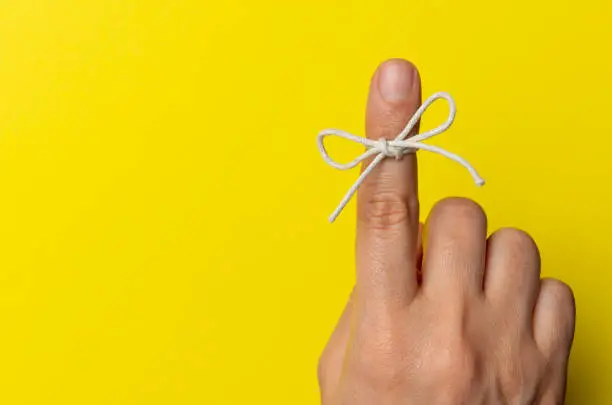Hand and string tied on index finger on yellow background.