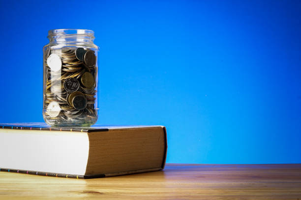 istock EDUCATION FUND CONCEPT with coins in a glass jar and old book. 1199147635
