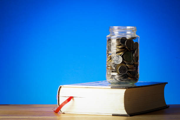 istock EDUCATION FUND CONCEPT with coins in a glass jar and old book. 1199147675
