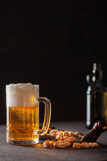 bicchiere di birra e pistacchi su un piatto su sfondo scuro - beer nuts foto e immagini stock