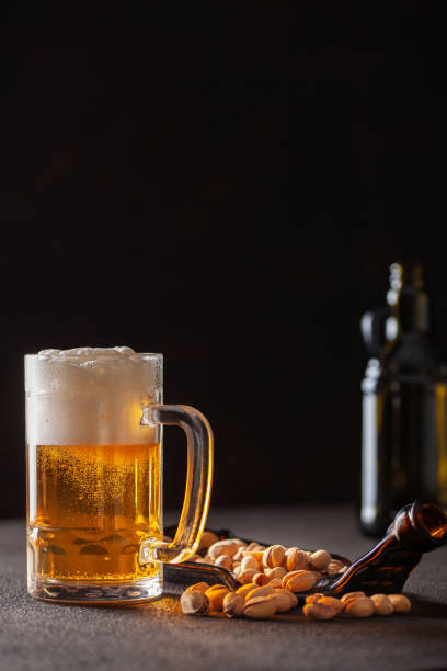 стакан пива и фисташки на тарелке на темном фоне - beer nuts стоковые фото и изображения