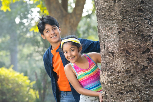 Girl and boy hiding and playing behind tree at park
