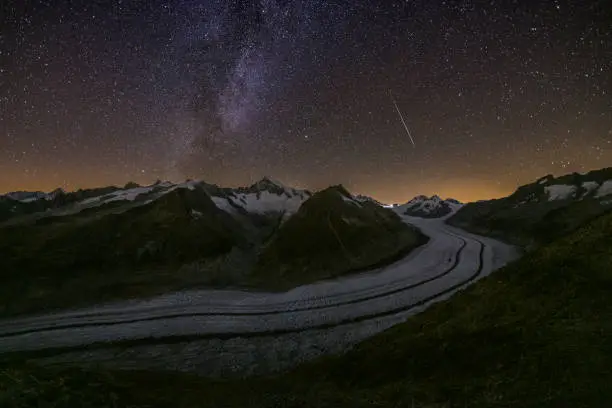 The Aletsch Glacier (German: Aletschgletscher) under the Milky Way at night. A meteor is visible on the right side of the sky. The Aletsch Glacier is the largest glacier in the European Alps and is located in Switzerland.