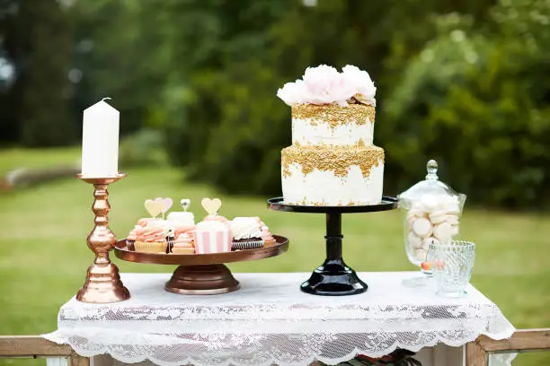 Cupcakes and a wedding cake on a sweet table closet outdoors on a meadow in shades of pink, white and gold